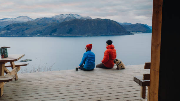Aerial view of woman and man contemplatoing a view of the scenic fjord during sunset relaxing in the shelter in Norway stock photo