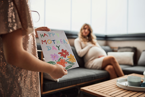 Beautiful girl is giving a card to her mom. It is mother’s day, so she drew a card to give to her. Happy mother's day! Woman is pregnant.