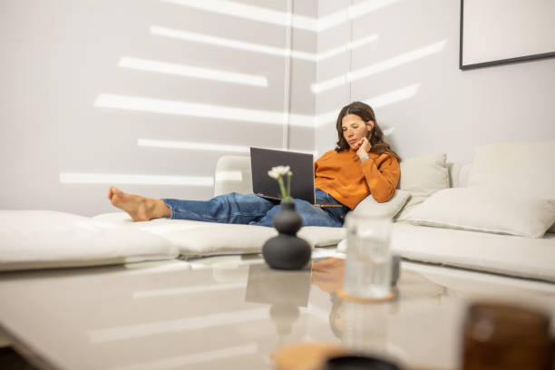 istock Beautiful young woman using laptop while relaxing on sofa at home 1447181583