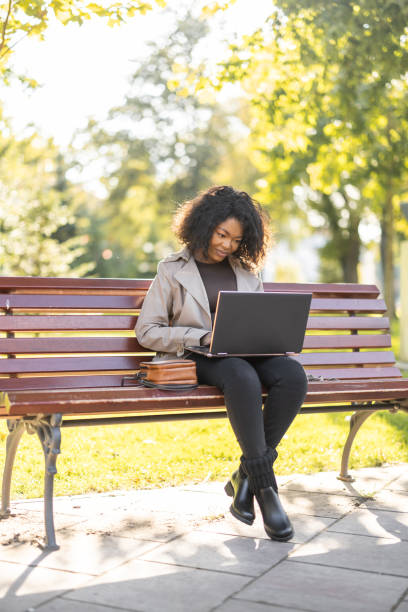 istock Young African woman using laptop outdoors on the park bench 1447183386