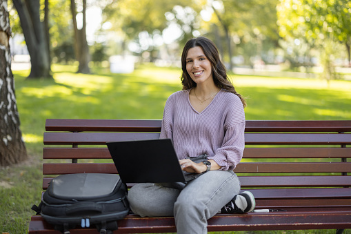 One young woman sitting on a bench in the park and using laptop on sunny day