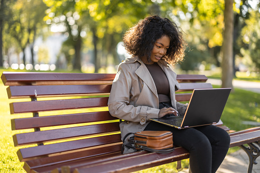 Young African woman using laptop outdoors on the park bench