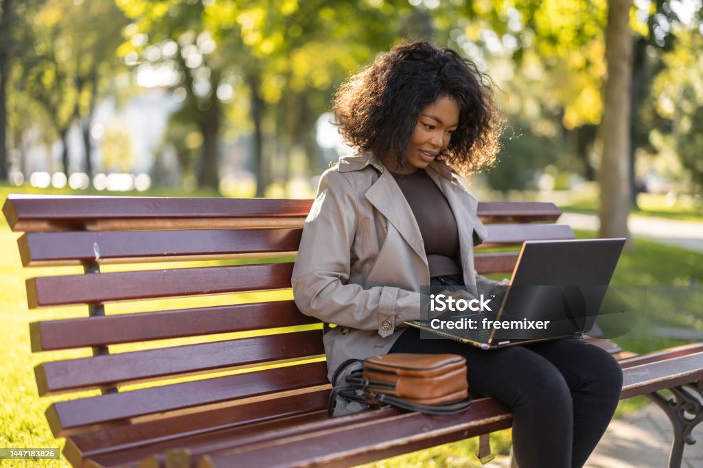 Young African woman using laptop outdoors on the park bench Laptop Stock Photo