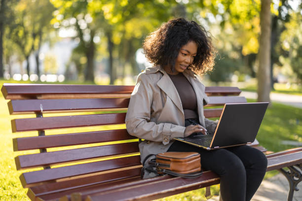 Young African woman using laptop outdoors on the park bench stock photo