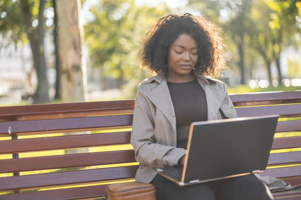 istock Young African woman using laptop outdoors on the park bench 1447183871