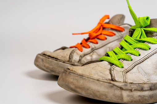 worn old torn white sneakers with colored laces on a white background. Close-up. Fashionable colored acid-colored shoelaces. side view from above
