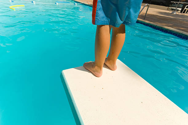 Child standing at the end of diving board Young box standing at the end of a diving board about to jump in.  Children playing in a swimming pool diving board stock pictures, royalty-free photos & images