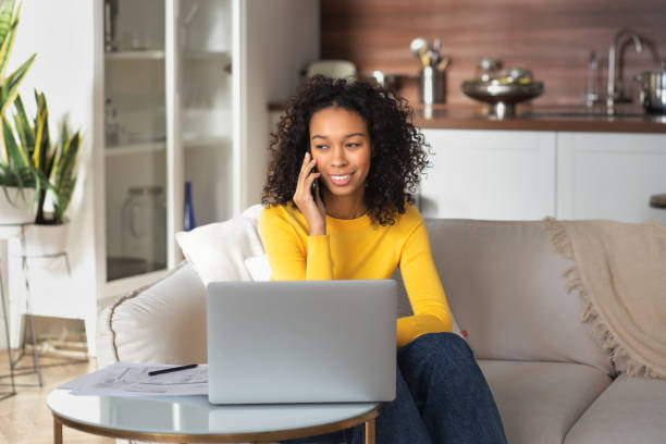 istock African American woman freelancer talking on a mobile phone, working working on new project online using a laptop sitting at home on the couch 1447188961