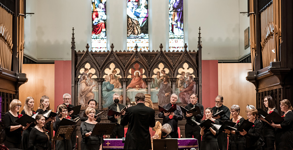 Church Choir during performance at Concert during Christmas Holiday season. Mixed age group of people dressed in all black attire. Interior of Anglican church at night.