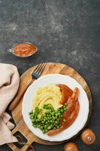 bangers und brei. gegrillte würstchen mit kartoffelpüree und grünen erbsen auf weißem teller auf schwarzem dunklem hintergrund. traditionelles gericht aus großbritannien und irland. bbq rindfleischwürste. draufsicht. - mashed potato food staple vertical color image stock-fotos und bilder