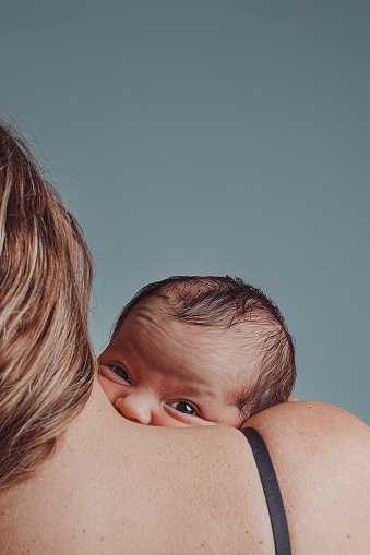 Newborn in his mother's arms looks at camera with sympathetic expression