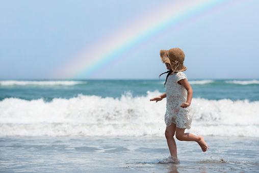 Little girl playing on the beach with a rainbow