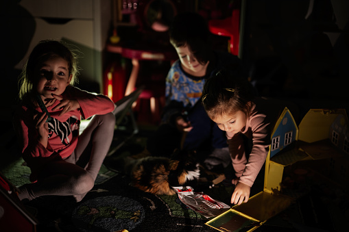 Children playing with kitty at home during a blackout using alternative lighting.