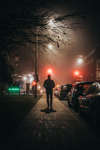 Man walking alone down a city street sidewalk on a foggy night. in Kingston, Ontario, Canada
