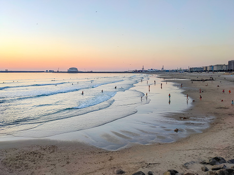 Matosinhos beach at susnet, people relaxing, cityscape and Leixoes port in background, Porto, Portugal