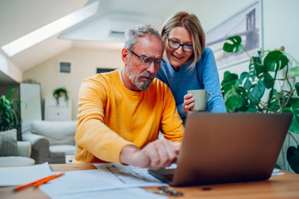 Senior middle aged happy couple using laptop together at home stock photo