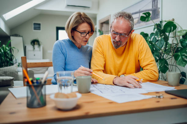 Senior couple sitting at table and looking into blueprints of their new home stock photo