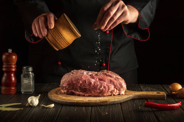 istock Professional chef sprinkles raw meat with salt. Preparing fresh meat before roasting. Menu concept for restaurant or hotel. Asian cuisine. 1447209733
