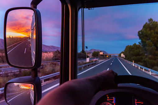 View of the highway from the driving position of a truck, with a dramatic sky sunset in the rear view mirrors.