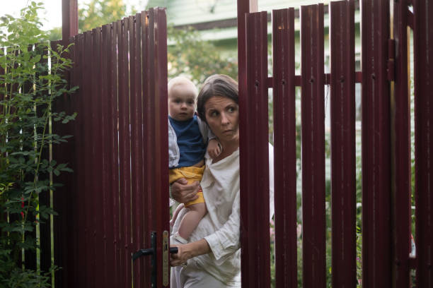 neugierige frau mit einem baby späht das tor des zauns auf - fence child neighbor peeking stock-fotos und bilder