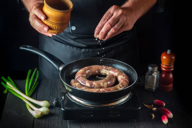 the chef adds salt to pan with raw meat sausage. preparation for cooking sausages in the kitchen of a restaurant or cafe on table with vegetables and spices - sausage food mash grilled imagens e fotografias de stock