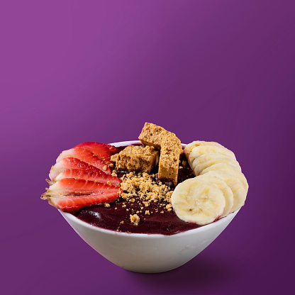 Brazilian Açai Bowl with Paçoca, Banana and Strawberry isolated on purple background.