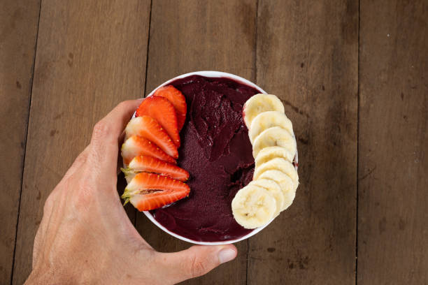 uomo che tiene una ciotola bianca di bacche di açai congelate brasiliane con banana e fragola. su una scrivania di legno. - men banana holding cut out foto e immagini stock