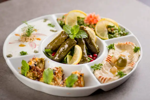 arabian mix starter with vine leaves, hummus, mezze, fatoush served in dish isolated on grey background top view of arabic food
