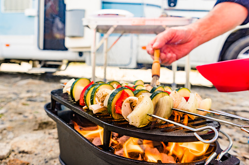 Assorted delicious grilled vegetable skewers on barbecue grill. Barbeque dinner outdoor. Rv camper in the background.