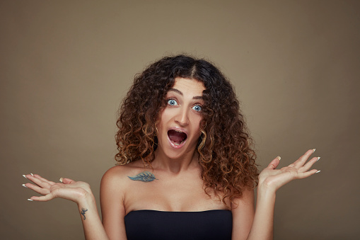 Portrait of young woman with curly hair with open arms, confused and screaming, blue eyes.