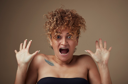 Portrait of young woman with curly hair with open arms, confused and screaming, blue eyes.