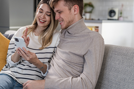 Young couple relaxing on the couch at home and looking at smartphone. Lifestyle and technology.