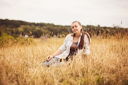 Portrait of a confident authentic young woman sitting in a field in the countryside