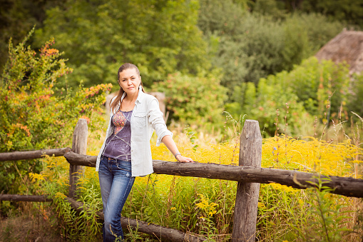 Attractive young woman casual wearing standing near old wooden fence.