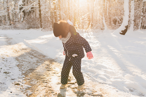 Girl in jacket and hat play in winter forest. Child. Happy childhood. Winter holiday. Deep snow. Girls. Warm clothes