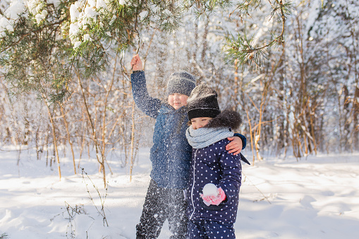 Girl and boy portrait in jacket and hat in winter forest. Children. Happy childhood. Winter holiday. Deep snow. Warm clothes
