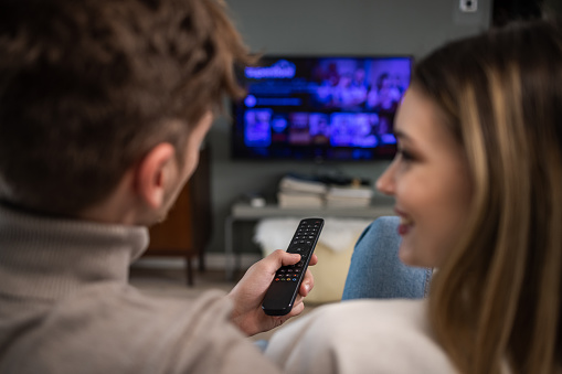 Rear view of cheerful couple smiling and talking while choosing a movie on TV. Togetherness. Bonding.