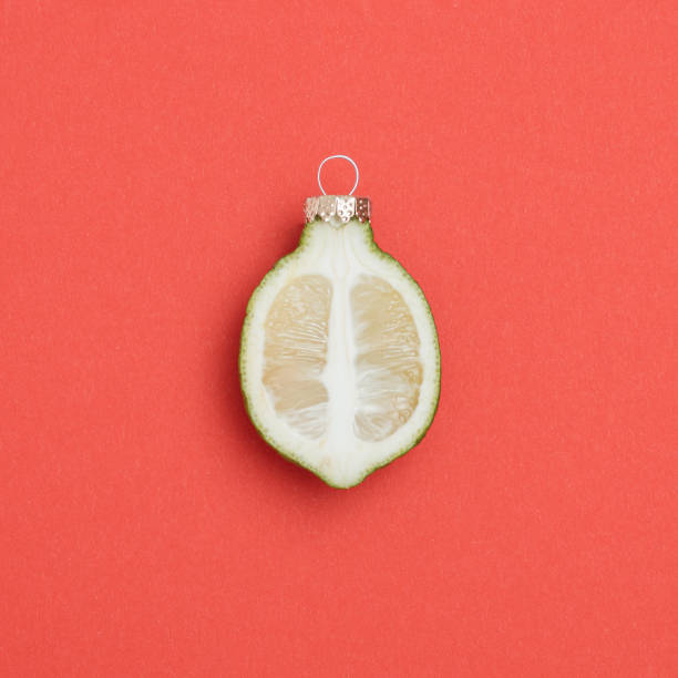 istock Sliced green lemon, line with Christmas bauble decoration on retro red background. Minimal Christmas concept. 1447234921