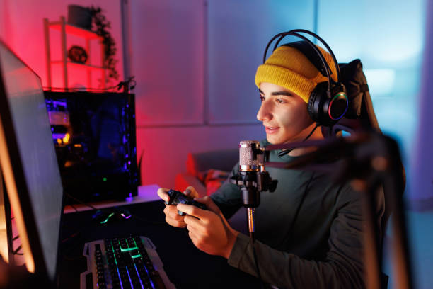 adolescente che gioca a giochi multiplayer su pc desktop nella sua dark room - streaming in diretta foto e immagini stock