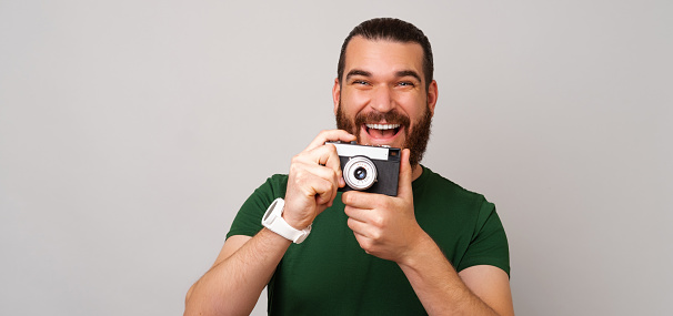 Banner size photo of a handsome man holding an old vintage photo camera. Studio shot over grey background.