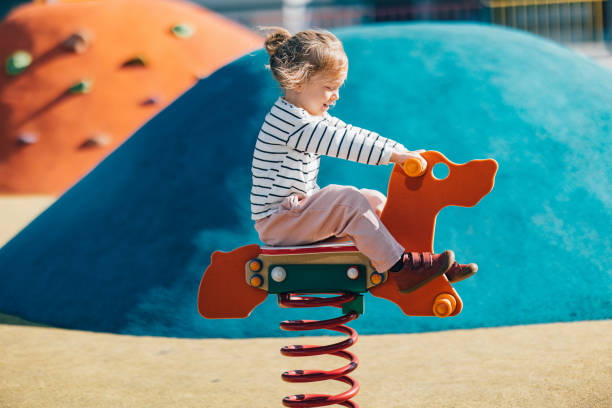 Little Girl Swinging On The Playground Side view of happy girl having fun while sitting on seesaw at outdoor playground. swinger photo stock pictures, royalty-free photos & images