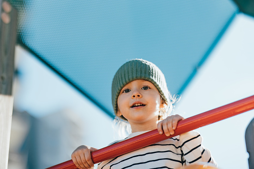 Low angle view of a smiling girl having fun while playing at outdoor playground and looking at camera.
