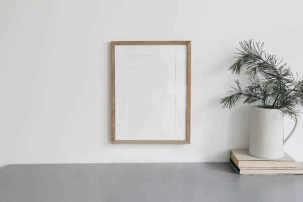 istock Christmas interior decor. Blank wooden picture frame mockup, white wall. Green pine tree branches in jug and old books. Grey working table. Old books. Winter home office still life. Poster display. 1447245071