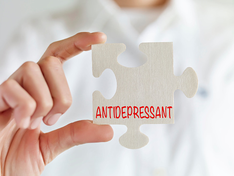 Doctor holding jigsaw puzzle pieces with “Antidepressant” text