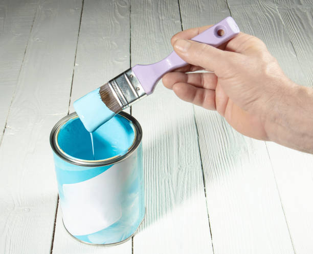 istock The hand holds a brush with a light blue paint flowing from it in a jar 1447249861