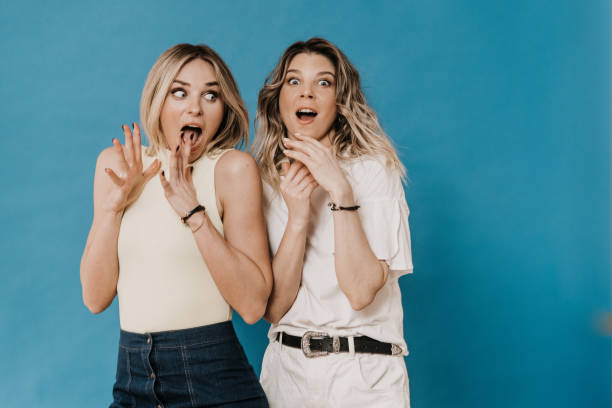 istock Two beautiful scared blondes screaming with their hands up, dressed in casual clothes on a blue background, news about new virus. People emotions concept. 1447255835