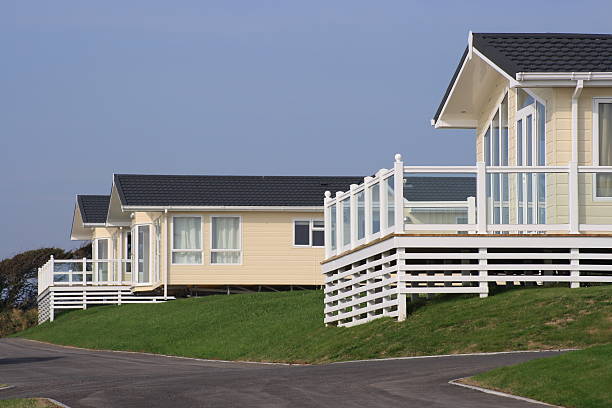 Three static holiday homes or caravans Three holiday homes perched on a grass bank with verandas and a road. manufactured housing stock pictures, royalty-free photos & images