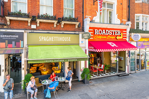 London, United Kingdom - June 22, 2018: Kensington high street road with people dining eating at sidewalk Italian pizzeria store cafe restaurant