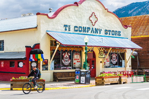 Crested Butte, USA - June 21, 2019: Colorado town street with pizzera restaurant cafe store shop at downtown in summer, man people riding bicycle bike