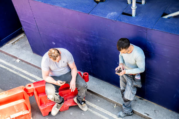 London, United Kingdom - June 22, 2018: Two construction workers men taking lunch break, using phones outside on street of city of Westminster